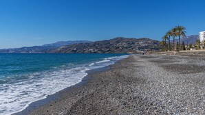A pebble beach with a clear blue sky, a calm sea, and distant mountains. - Apartment 'Bonito Apartamento Frente Al Mar' with Sea View, Wi-Fi and Air Conditioning (Salobreña)