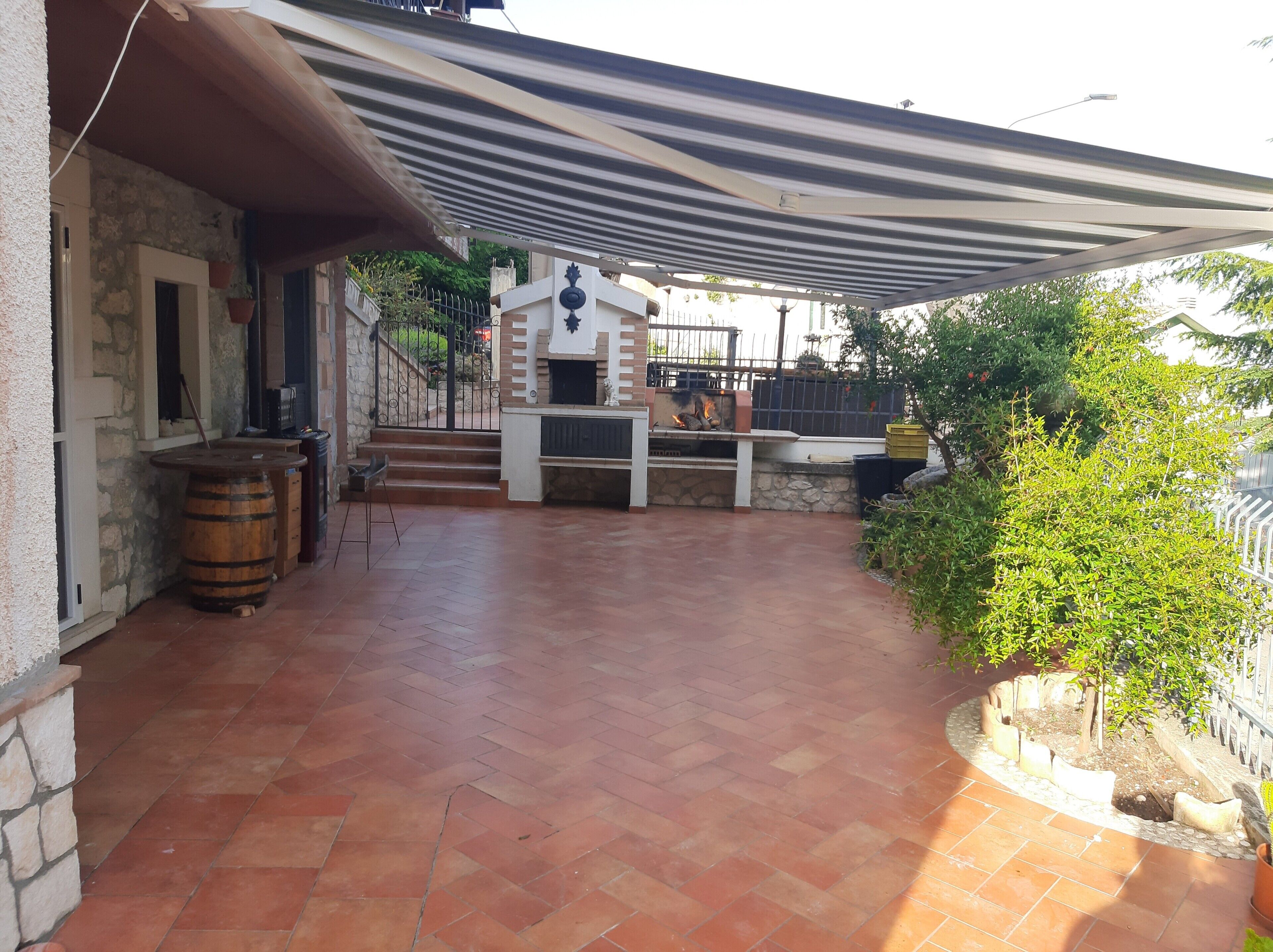 Eine Terrasse mit Grillplatz, Steinmauern und einem Streifenmarkisen.