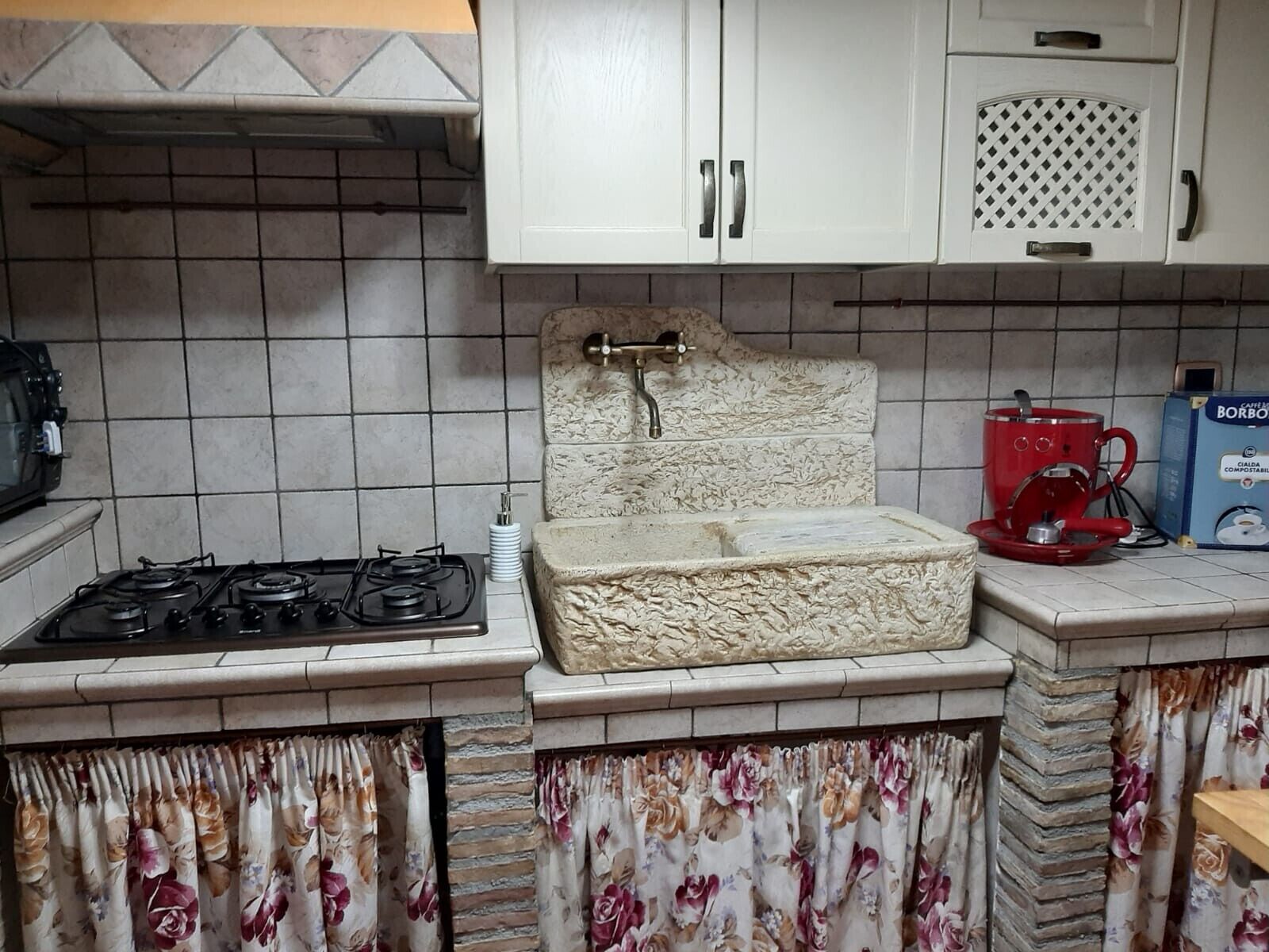 A kitchen with a gas stove, a sink with a decorative stone backsplash, and a coffee machine.