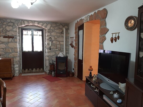 Un salon avec un mur en pierre, une porte en bois, un téléviseur et une cheminée.