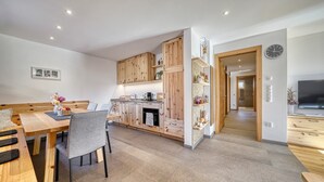 Een moderne keuken met houten kastjes, een eetgedeelte met een bank, en een televisie in de woonkamer.