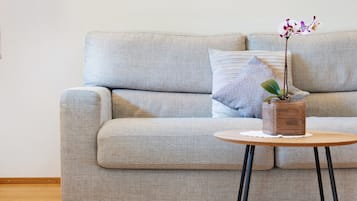 A grey sofa with a small round wooden table and a potted orchid.