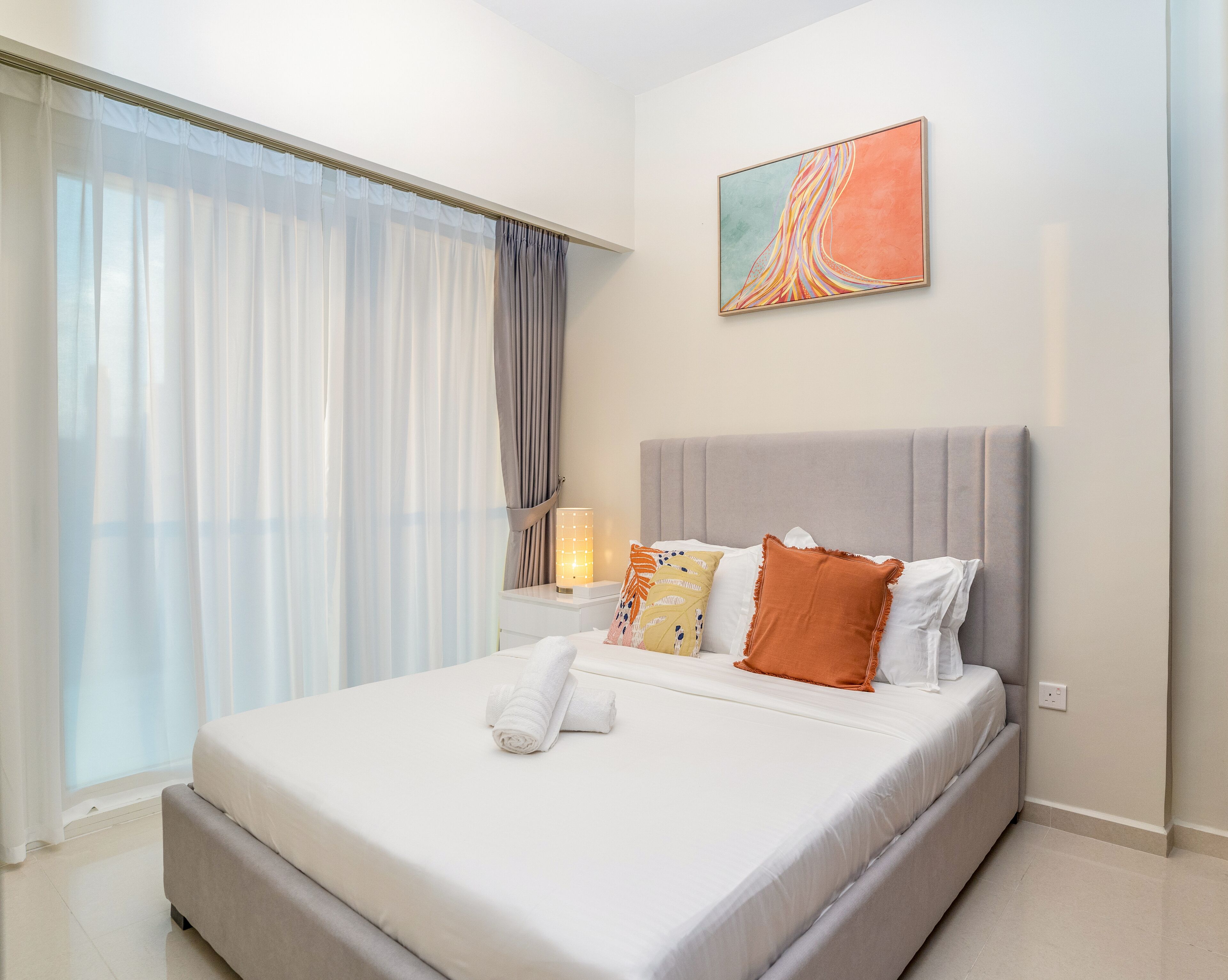 A modern hotel room with a large bed, a bedside table with a lamp, and a painting on the wall.