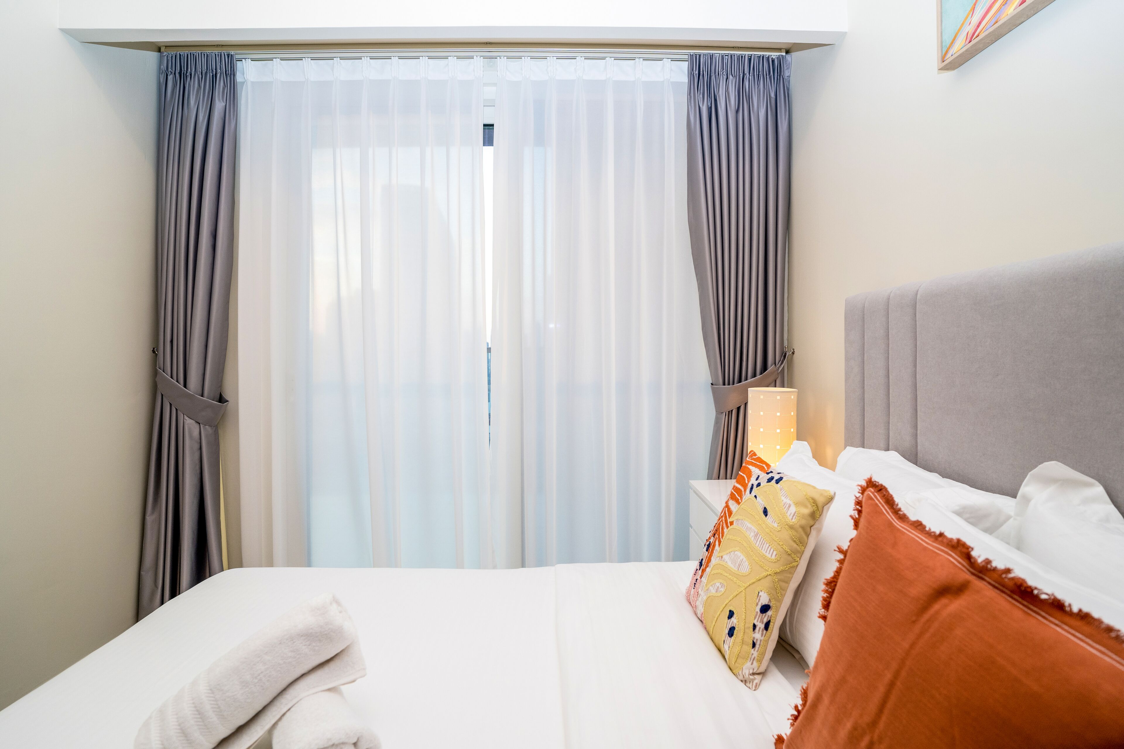 A hotel room with a bed, a nightstand, a lamp, and a window with curtains.