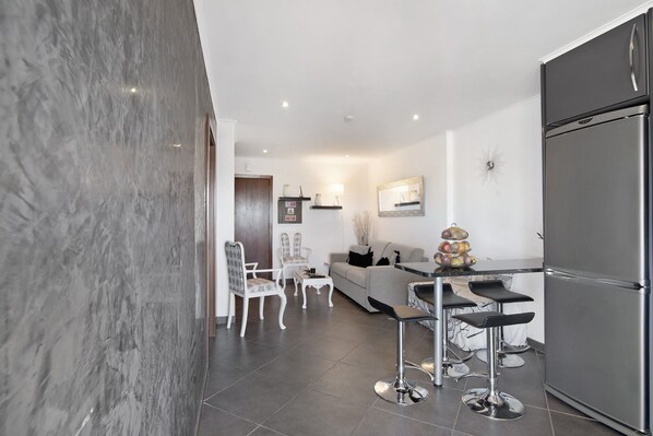 A modern kitchen with a large refrigerator, bar stools, a dining table, and a sofa.