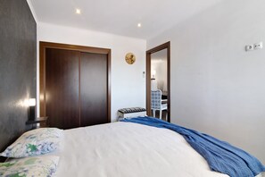 A bedroom with a bed, a wardrobe, a chair, a small table, and a wall clock.