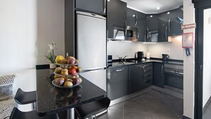 Una cocina moderna con electrodomésticos de acero inoxidable, una encimera negra y una exhibición de frutas.