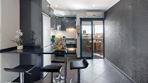 Cocina moderna con una isla central, taburetes de bar y vistas de la ciudad a través de una puerta abierta.