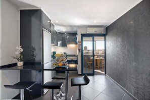 A modern kitchen with a central island, bar stools, and a view of the city through an open door. - Apartment 'Apartamento Freire' with Balcony, Wi-Fi and Air Conditioning (Portimão)