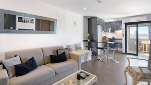 Una sala de estar moderna con un sofá, una mesa de centro y un comedor con sillas, y una cocina al fondo.