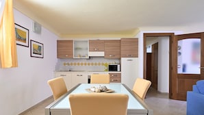 Un coin repas avec une table en verre, quatre chaises, une cuisine en arrière-plan et un canapé bleu.