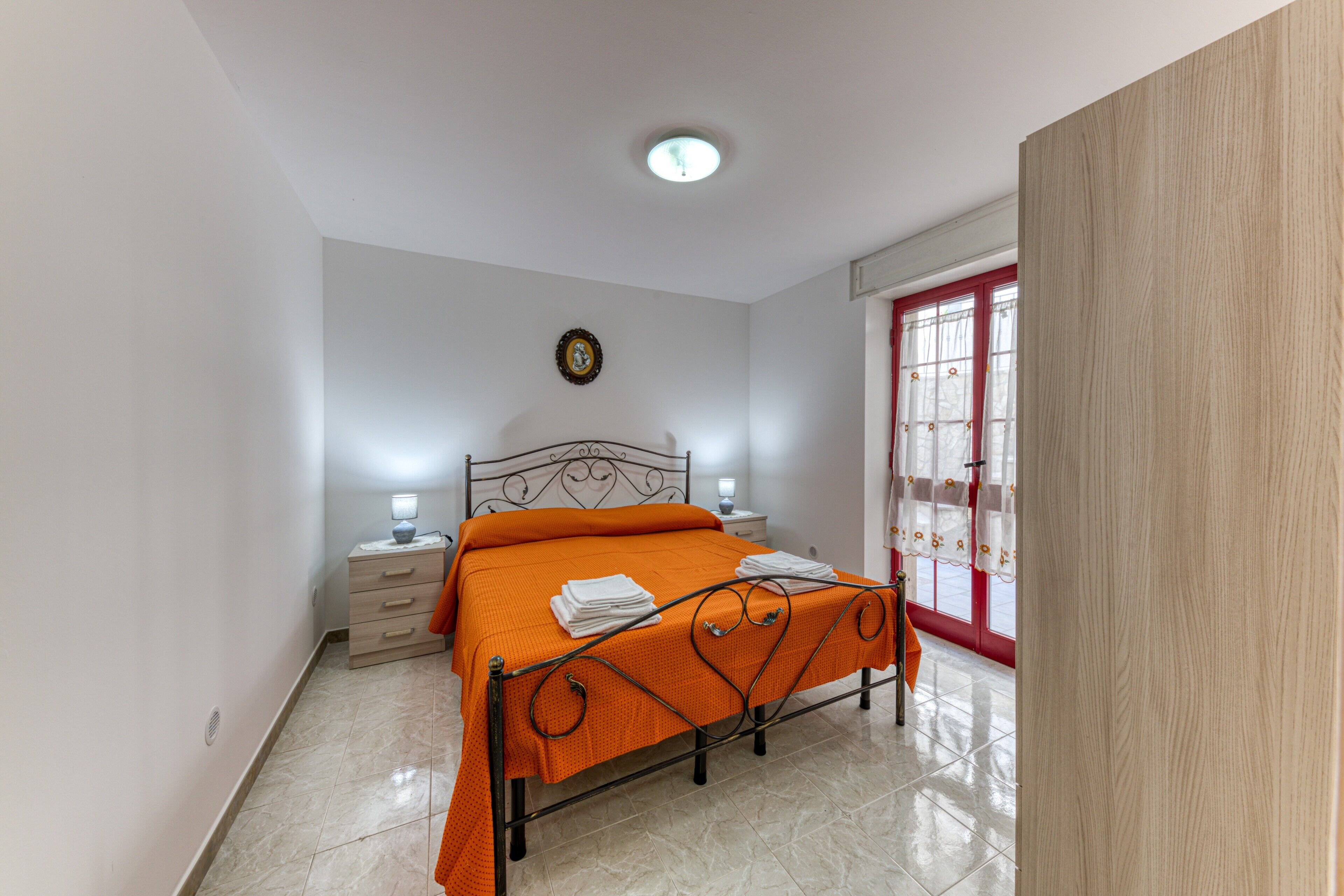 A bedroom with a bed, bedside tables, a nightstand, a wall clock, and a window with curtains.