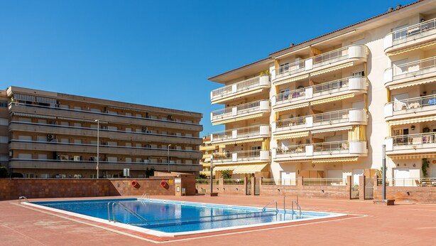 A swimming pool area with a building featuring multiple balconies and a tiled roof. - Apartment "Blanes" close to the Sea with Shared Pool (Blanes)