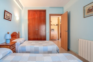 A bedroom with a wooden wardrobe, a bed with a checkered duvet, a bedside table with a lamp, and a framed picture on the wall. - Apartment "Blanes" close to the Sea with Shared Pool (Blanes)