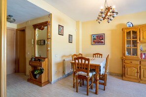 Un coin repas comprenant une table en bois, des chaises, un lustre, un buffet aux portes vitrées et un radiateur.