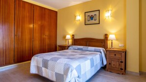 A bedroom with a bed, wooden wardrobe, two bedside tables with lamps, and a wall-mounted light fixture. - Apartment "Blanes" close to the Sea with Shared Pool (Blanes)