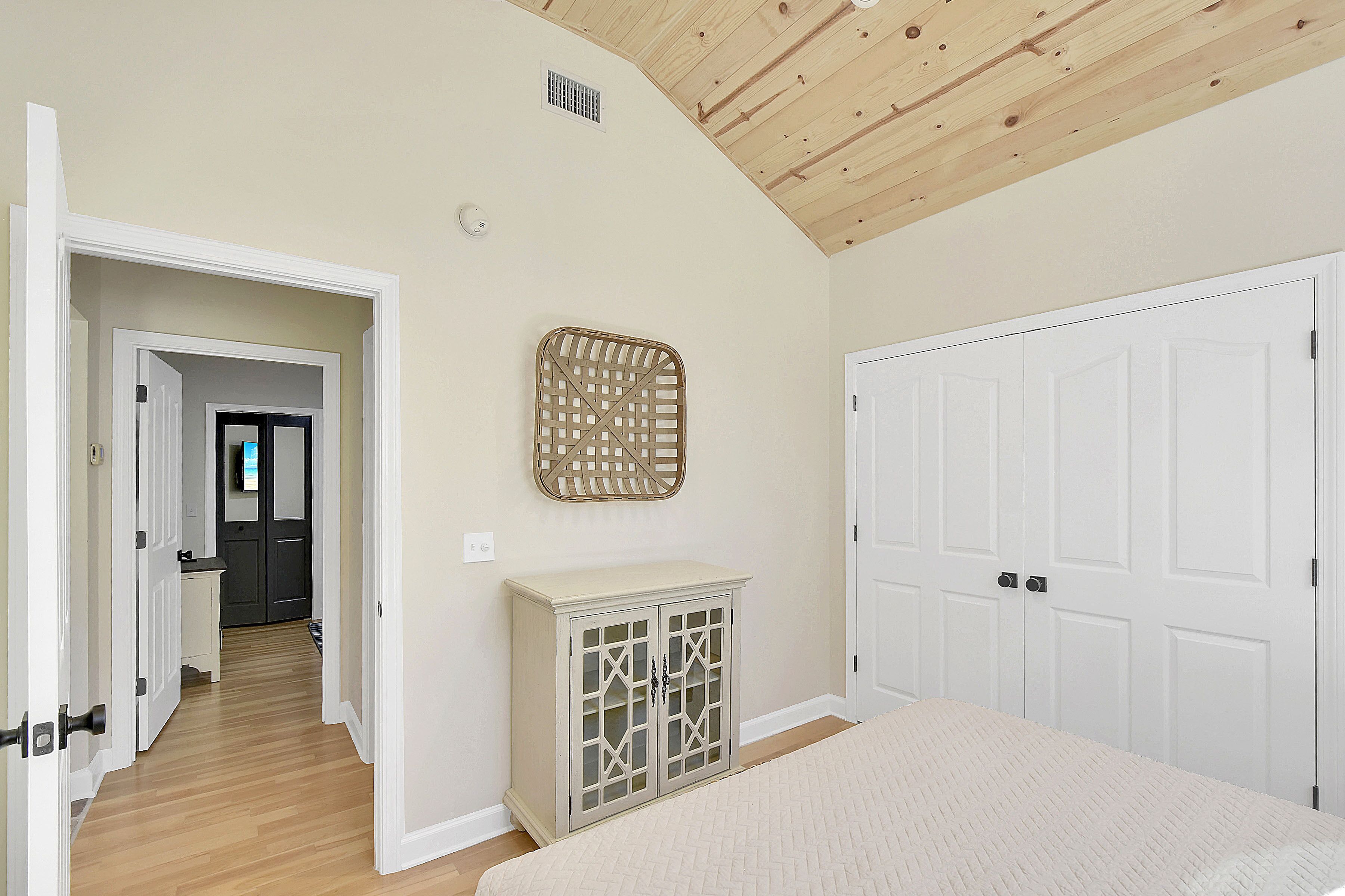 Un dormitorio con techo de madera, una cama, un armario y una puerta que da a otra habitación.