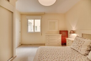 Un dormitorio con cama, mesita de noche, cómoda, ventana y puerta.