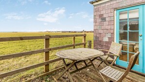 Una terraza de madera con una mesa y sillas, una puerta azul y vista a un campo cubierto de césped.