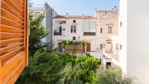 A courtyard with a wooden door, a white building with a balcony, and lush greenery. - Alchemy Apartment (Conversano)