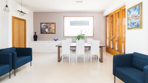 A modern dining area with a white table, chairs, and pendant lighting. There are two blue sofas and a wooden cabinet with decorative items. - Alchemy Apartment (Conversano)