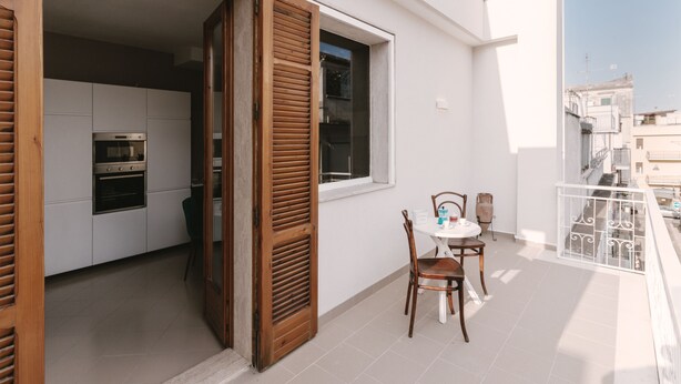 An open wooden door leading to a kitchen with white cabinets and a built-in oven. - Alchemy Apartment (Conversano)