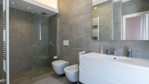 Un baño moderno con mampara de ducha de vidrio, un bidé, un lavabo grande y un espejo.