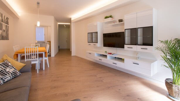 Una sala de estar moderna con un sofá, una mesa de comedor, sillas y un mueble para la televisión.