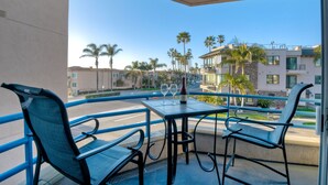 A balcony with a table and chairs, a bottle of wine, and a view of palm trees and buildings. - Ocean View, Pool, Hot Tub, Steps To Pier, Gated (Oceanside)