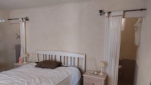 Una camera da letto con un letto, comodini, uno specchio e un bagno parzialmente visibile dietro una tenda.