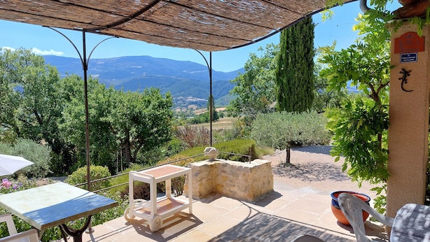 Un patio con tavolo e sedie, un piccolo carrello e vista sulle montagne e sul verde.
