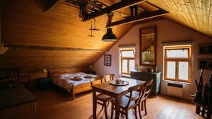 Une chambre confortable située sous les toits, avec un plafond en bois, un lit, une table à manger et deux fenêtres.