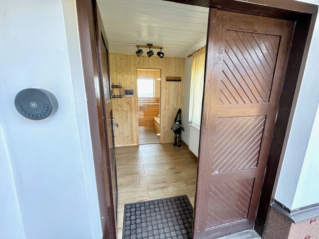 A wooden interior hallway with a door, a doormat, and a staircase leading to another room.