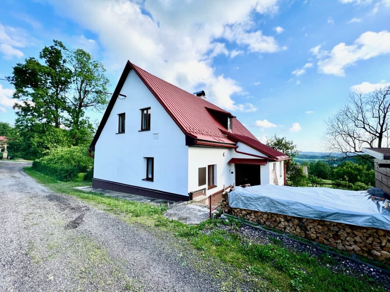 A white house with a red roof, a gravel driveway, and a stone wall.