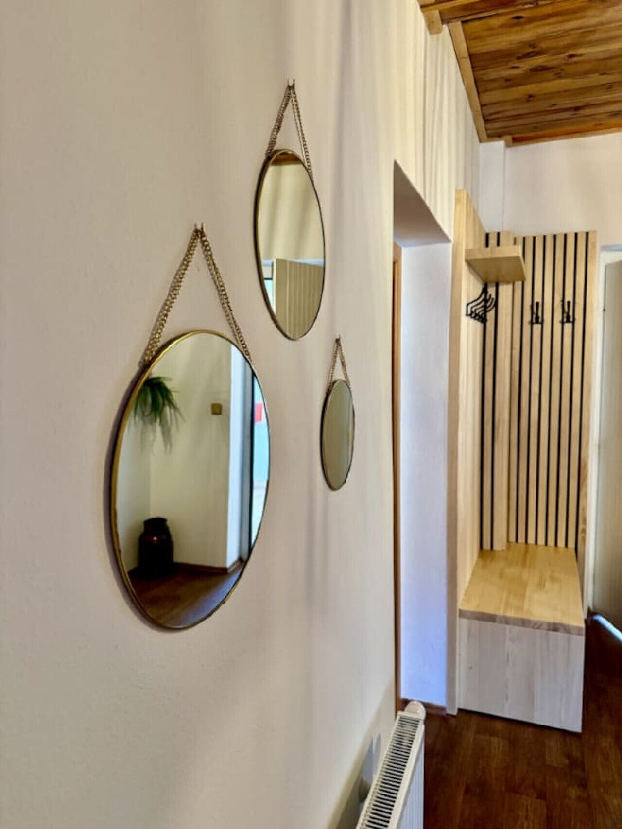 A hallway with three oval mirrors on the wall, a wooden bench, and a vertical wooden slat wall.