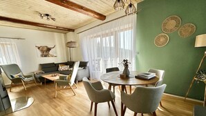 En rummelig stue med trægulv, et rundt spisebord med stole, en sofa og et sofabord.