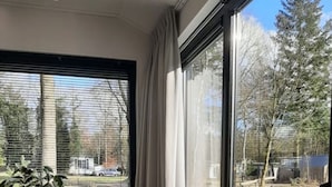 Una habitación moderna con una mesa de comedor y sillas, ventanas amplias con cortinas y vistas a un paisaje verde y árboles.