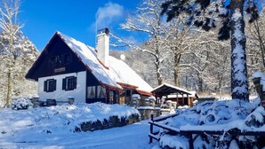 Un chalet enneigé, doté d’une cheminée imposante, d’une terrasse en bois et d’une façade rustique.