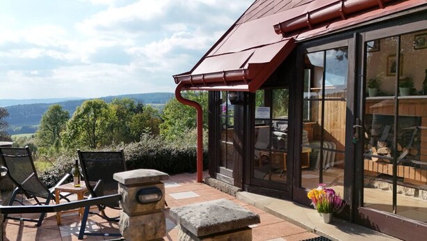 Une terrasse avec des sièges extérieurs, un pilier en pierre et une vue sur le paysage.