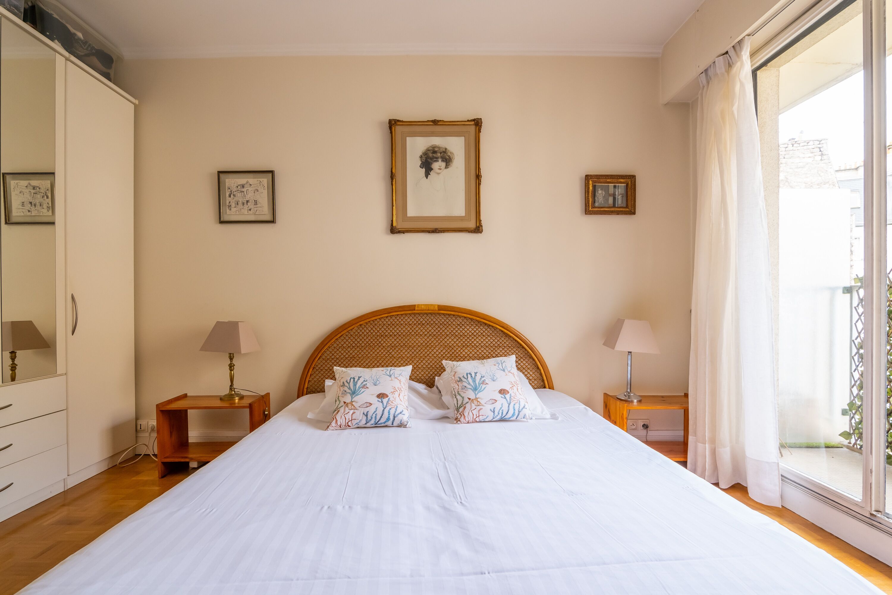 A bedroom with a large bed, two bedside tables with lamps, a wardrobe, and framed pictures on the wall.
