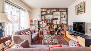 A living room with a sofa, armchairs, a coffee table, a bookshelf, and a TV.