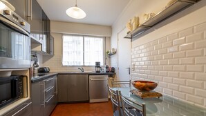 A modern kitchen with stainless steel appliances, a glass dining table, and a white tiled backsplash.