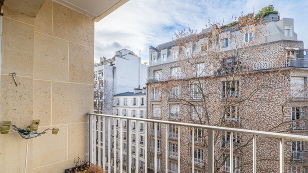 A balcony with a tiled wall, a potted plant, and a view of adjacent buildings.