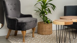 A modern living room with a dark grey armchair, a round wooden table, a potted plant, and a large abstract painting on the wall. - Modern 1-Bedroom With Wetland Views | Netflix (Cape Town)