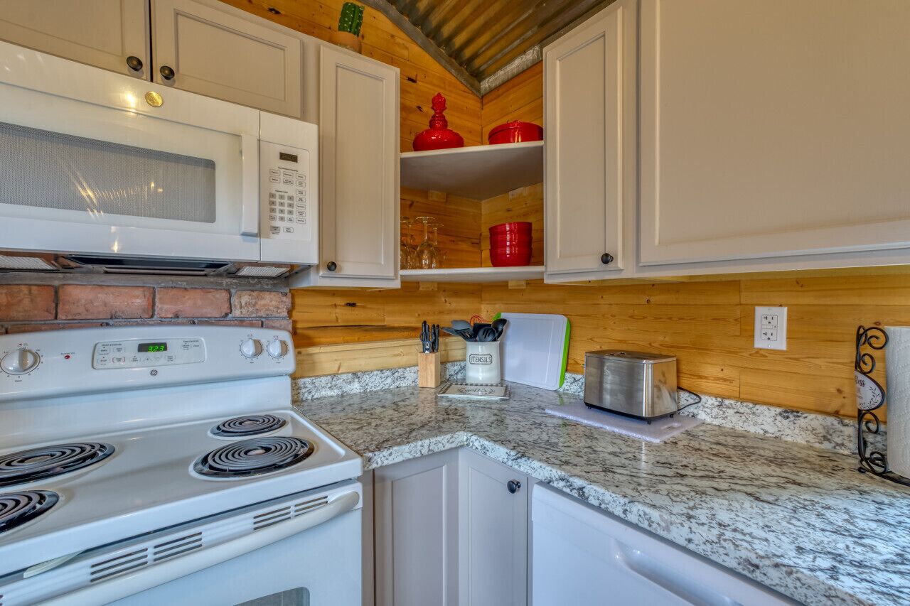 A kitchen with white cabinets, a white stove, a microwave, and red storage containers.