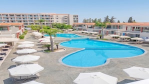 A hotel with multiple swimming pools, outdoor seating, and a building with a tiled roof. - Sun Palace Protaras Waterpark Resort (Paralimni)