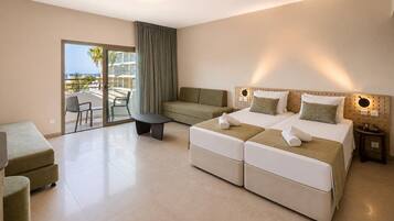 Habitación de hotel con balcón, sofá, cama con dos almohadas, una mesita y un buró.