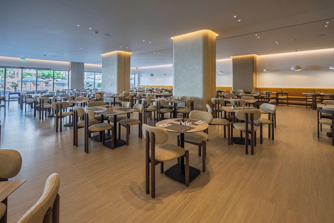 Un restaurante espacioso con numerosas mesas y sillas, grandes pilares y vistas al exterior.