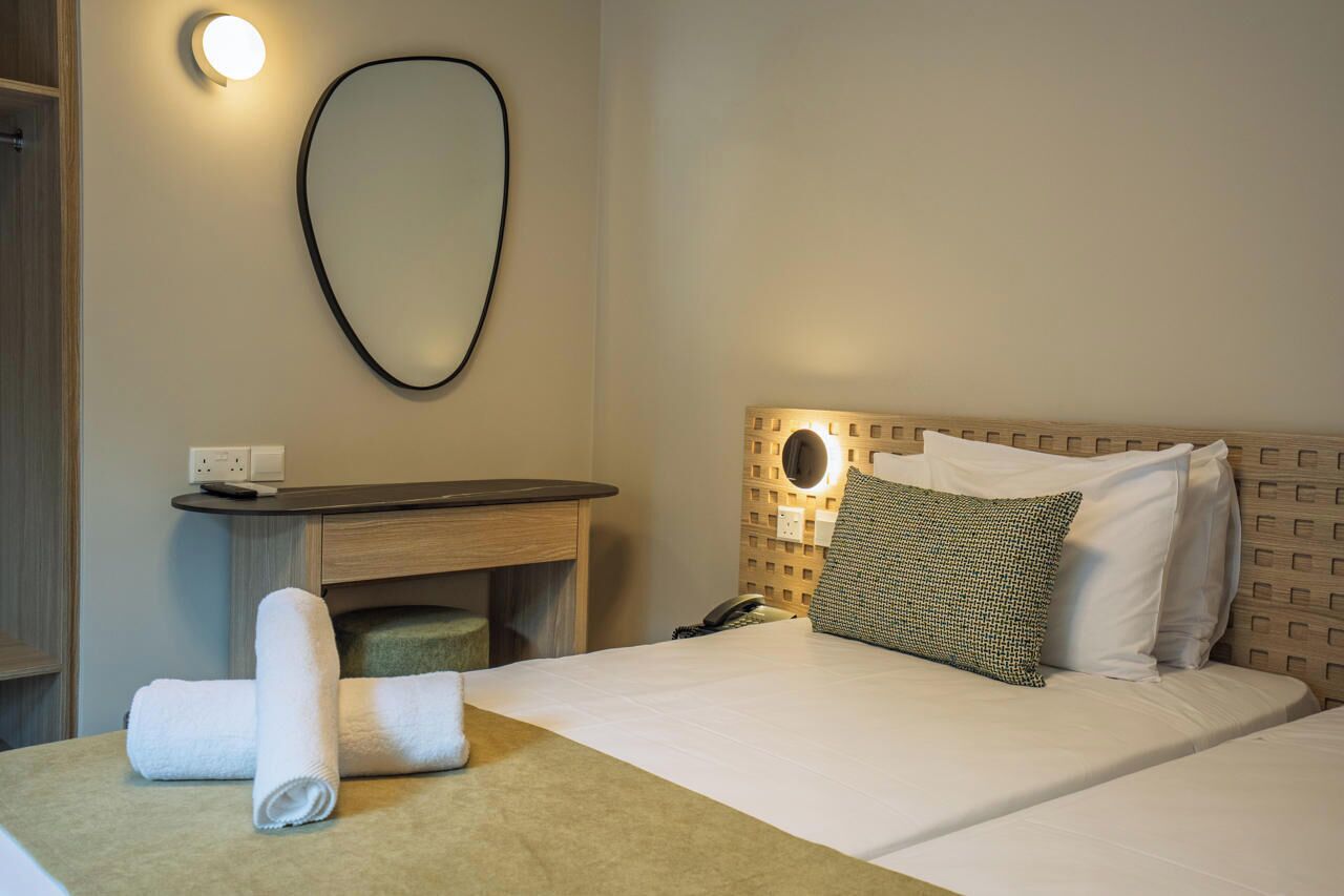 A hotel room with a bed, a bedside table, a lamp, and a wall-mounted mirror.