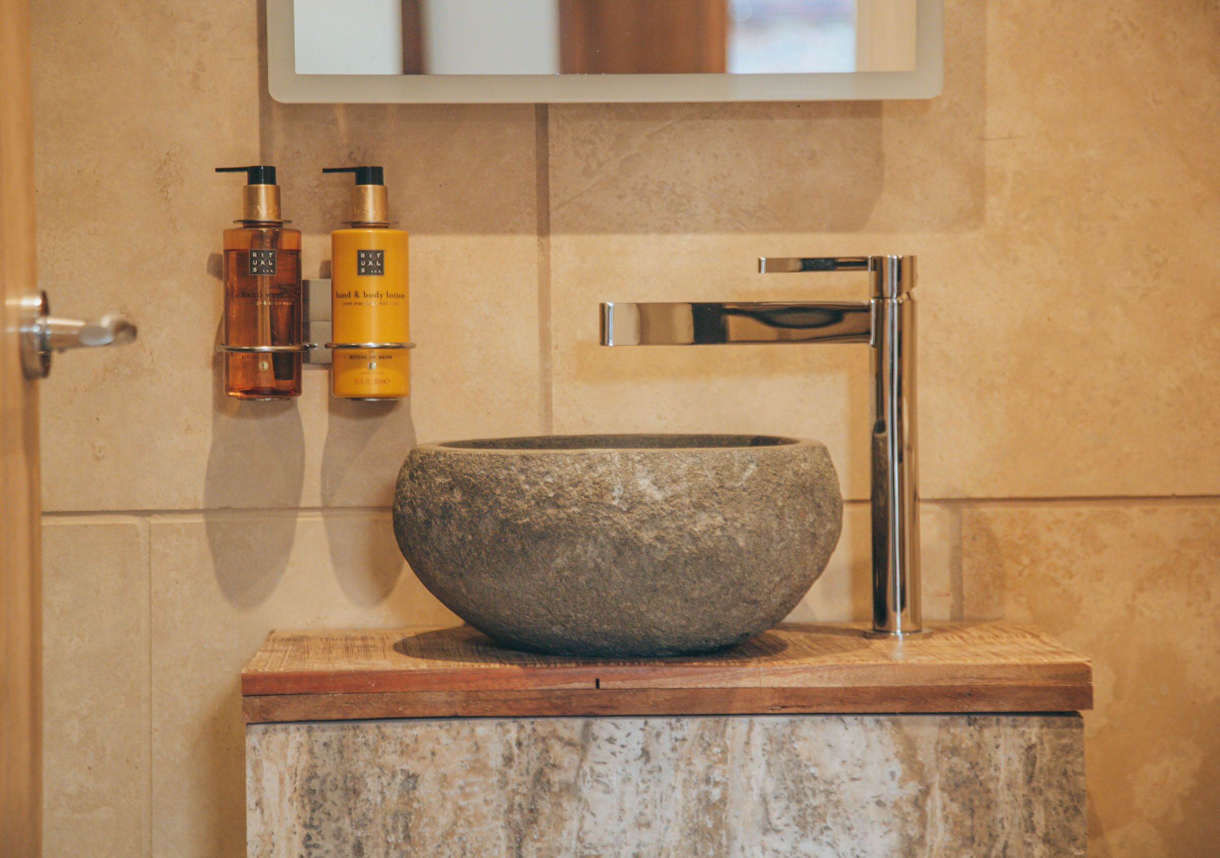 Un baño con un lavabo de piedra, un grifo de cromo y dos botellas de loción en la pared.